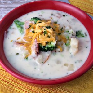 Red bowl with Slow Cooker Bacon and Broccoli Soup topped with cheddar cheese.